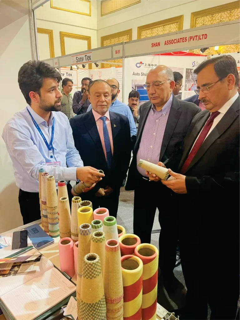 A group of four men at a trade exhibition, discussing paper cones while standing around a table displaying various cone types.